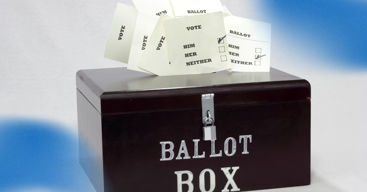 A ballot box with several paper ballots labeled 'Vote' and checkboxes for options such as 'Him,' 'Her,' and 'Neither,' illustrating the voting process and teaching civic responsibilities in an election setting.