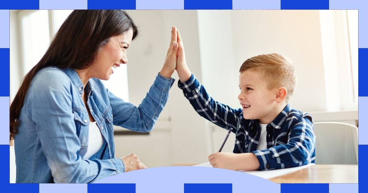 A smiling woman and a young boy sitting at a table, giving each other a high-five during a homeschooling session, with sunlight streaming through the window in the background.