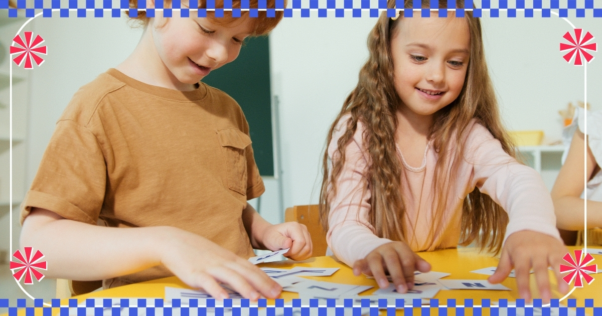 Two children smiling and playing with flashcards on a yellow table, engaged in a fun learning activity, with a colorful decorative border featuring a checkered pattern and red pinwheel accents.