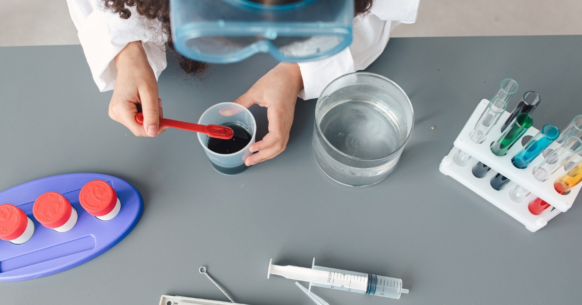 A child conducting a science experiment at home, wearing safety goggles, using a dropper and colored liquids with test tubes and other lab equipment on a table, illustrating hands-on learning in a homeschool environment.