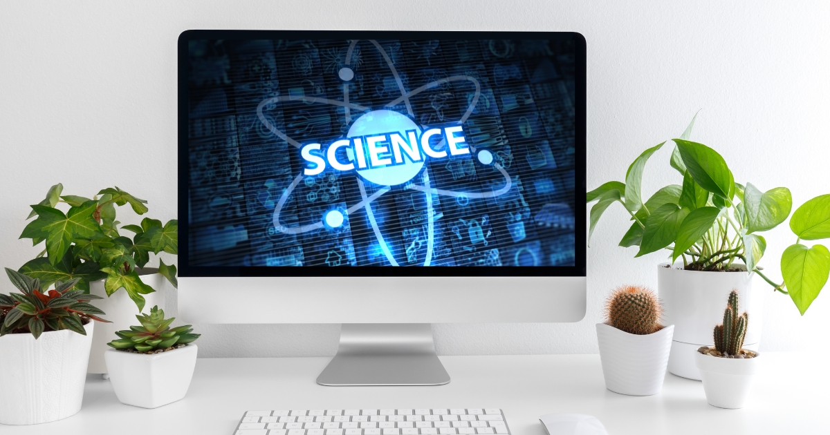 A modern desktop computer displaying the word 'SCIENCE' with an atomic design on the screen, surrounded by green plants and cacti on a clean, white desk.