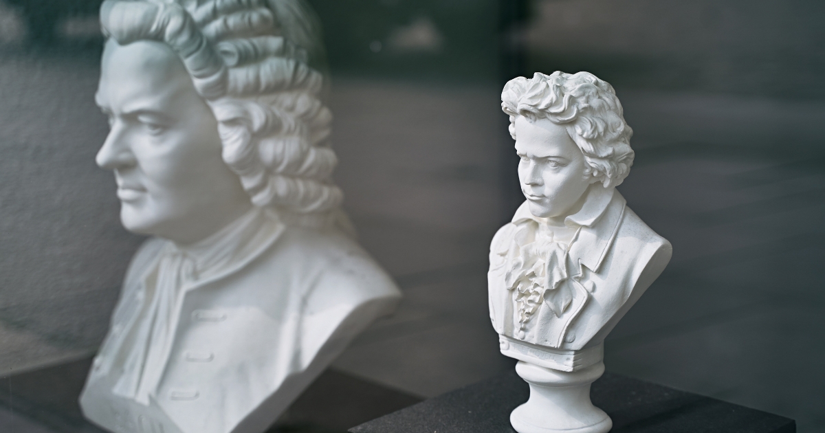 White marble busts of two classical composers, one in the foreground and the other reflected in glass, symbolizing the legacy of classical music.