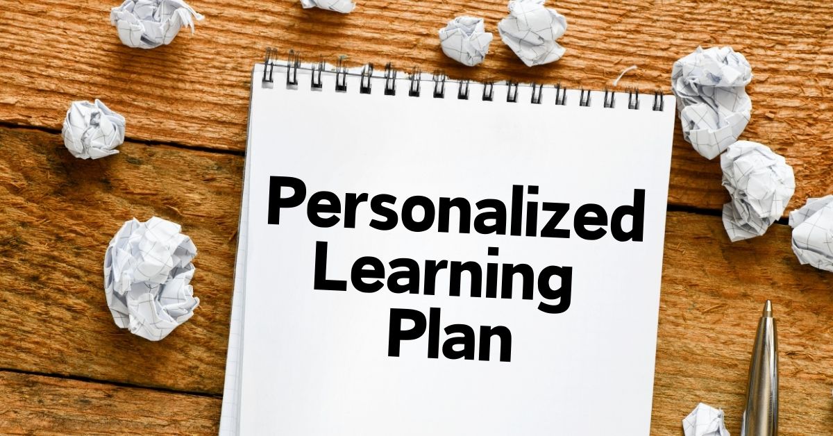 Notebook with 'Personalized Learning Plan' written in bold black text, placed on a wooden surface with crumpled paper balls and a pen nearby.