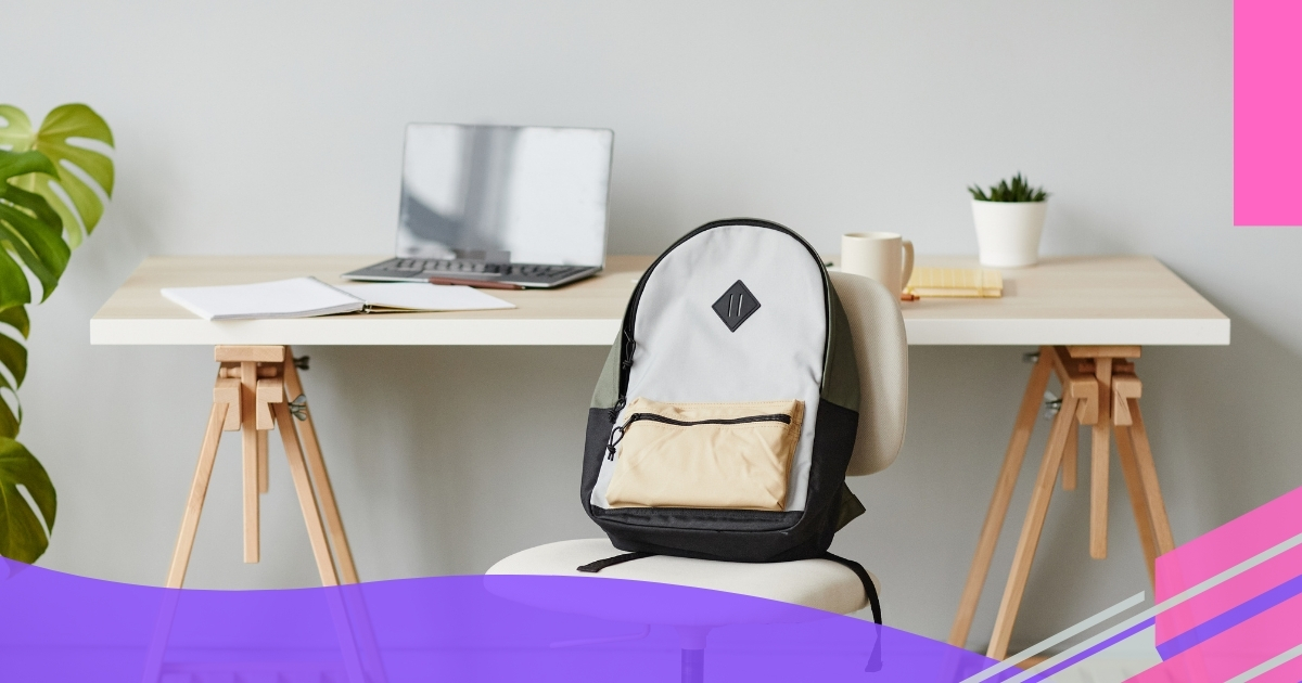 Homeschool setup featuring a desk with a laptop, open notebook, coffee mug, and a small plant, with a backpack resting on a chair in a minimalist home office setting.