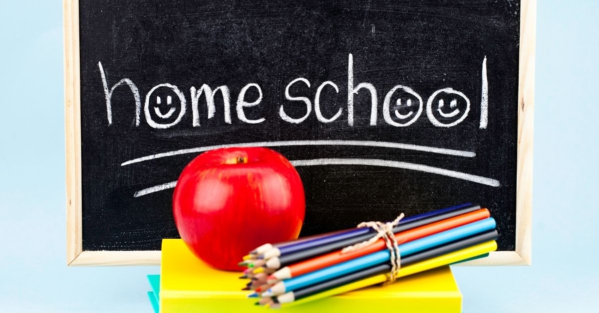 Chalkboard with 'home school' written in white chalk, featuring smiley faces, alongside a red apple, colorful pencils, and stacked books on a light blue background.