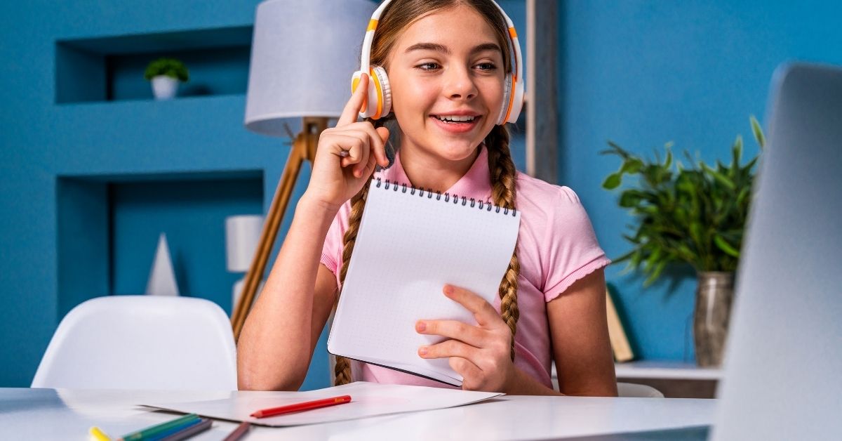 Happy homeschooled girl learning online with headphones and notebook.