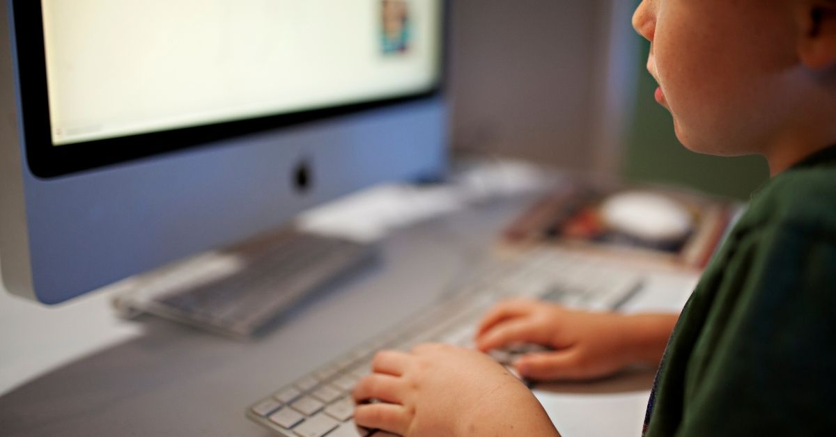 Close-up of a young child using a computer keyboard, focused on an educational activity on a desktop screen.