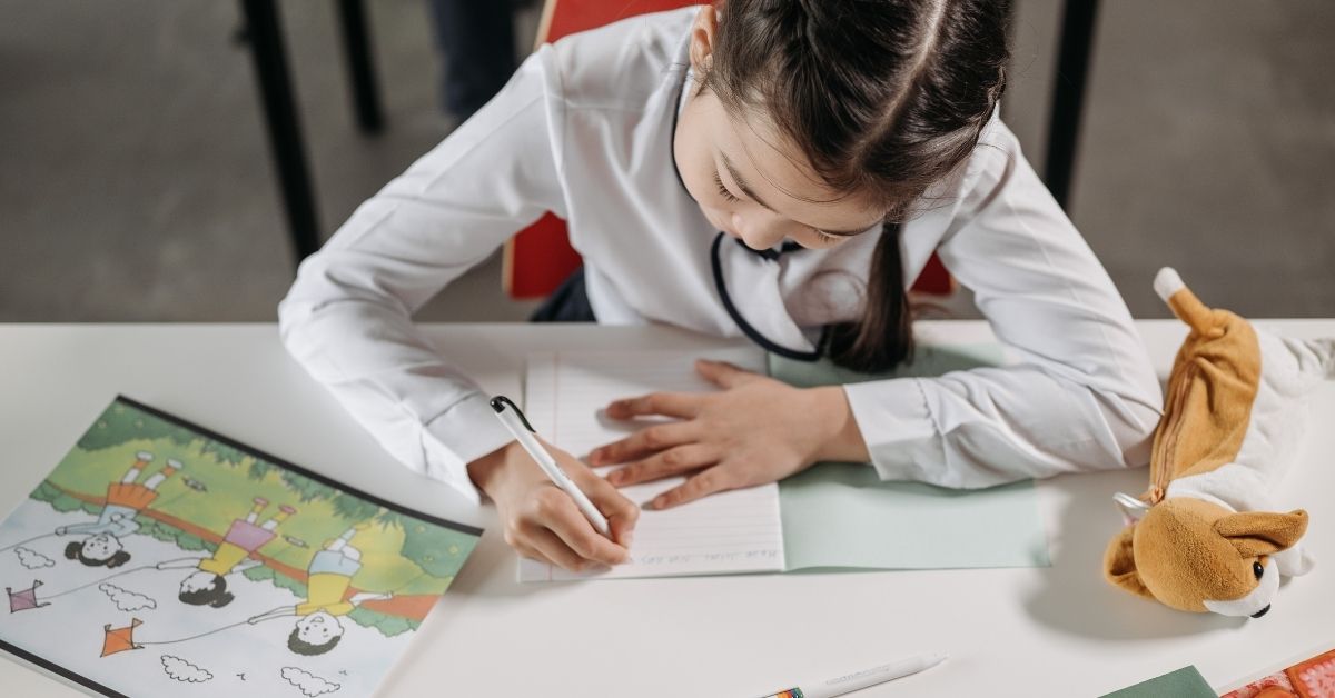 oung girl practicing writing at a Montessori homeschool desk, engaging in independent learning with a notebook and educational materials.