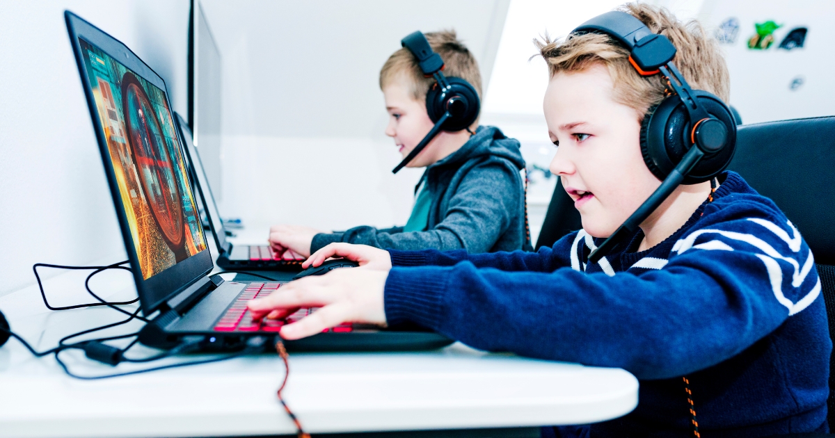 Two young boys wearing gaming headsets, engaged in an educational video game on laptops, demonstrating the use of gamified learning in homeschooling.