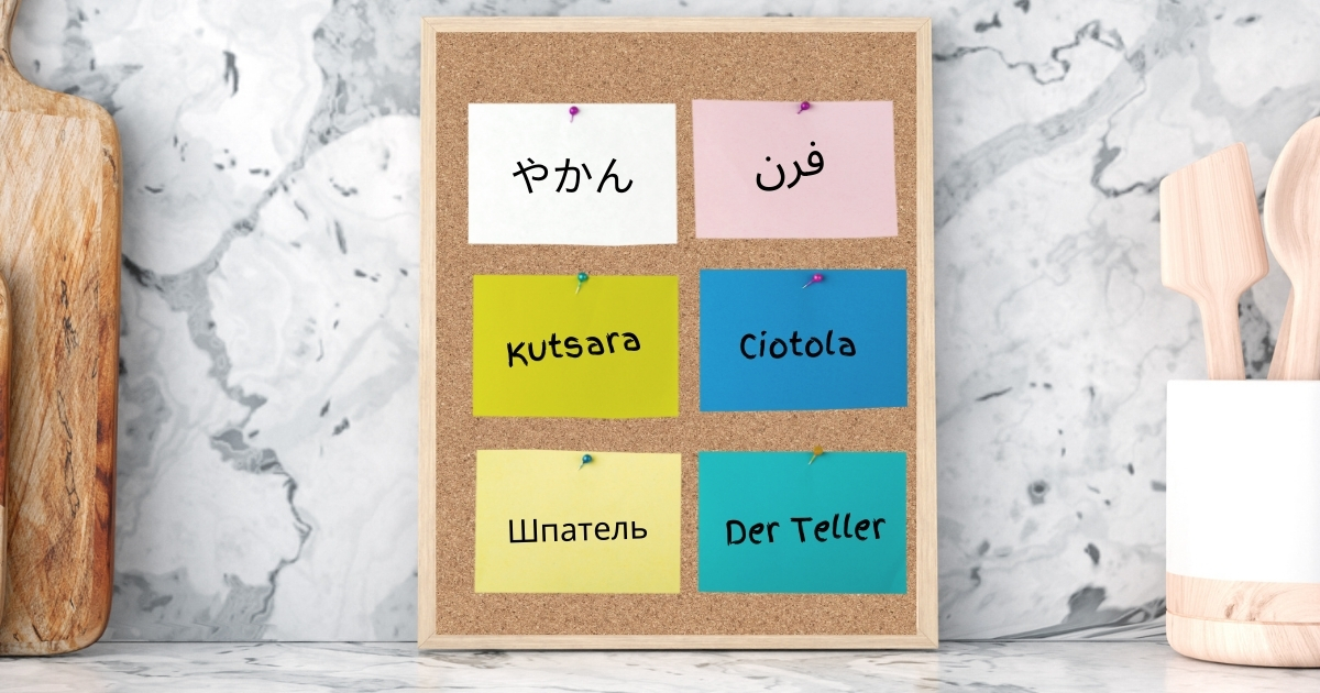 Multilingual word labels pinned on a corkboard for Montessori foreign language learning, featuring words in Japanese, Arabic, German, Italian, Russian, and Filipino.