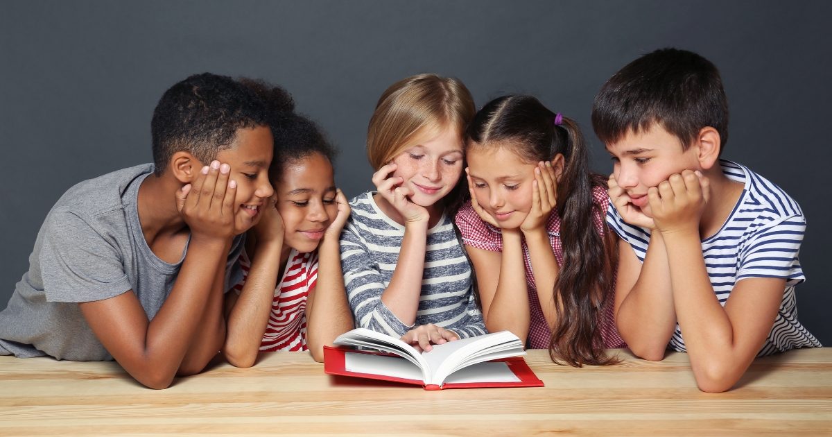 Diverse group of children engaged in reading a book together, illustrating the Charlotte Mason approach to literature and fostering a love for reading through shared storytelling.