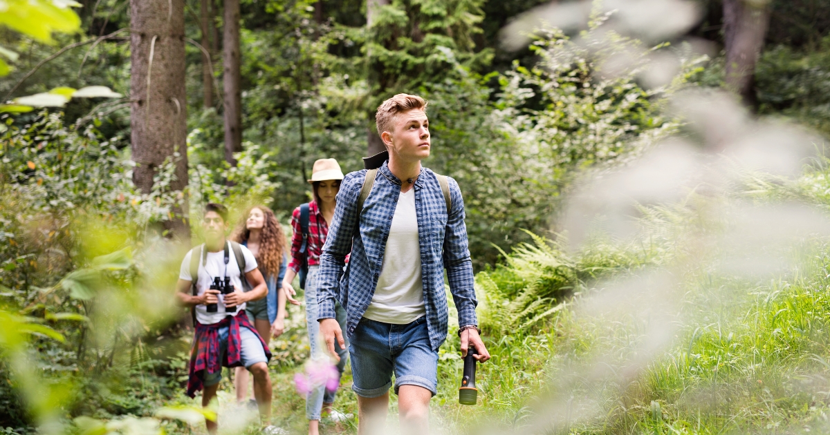 Group of teenagers exploring a forest on a nature hike, demonstrating hands-on geography learning through the unschooling approach.