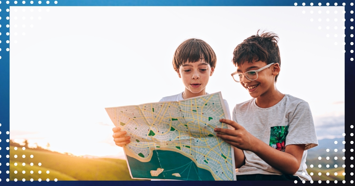 Two children exploring a map outdoors, demonstrating hands-on geography learning through the unschooling approach.