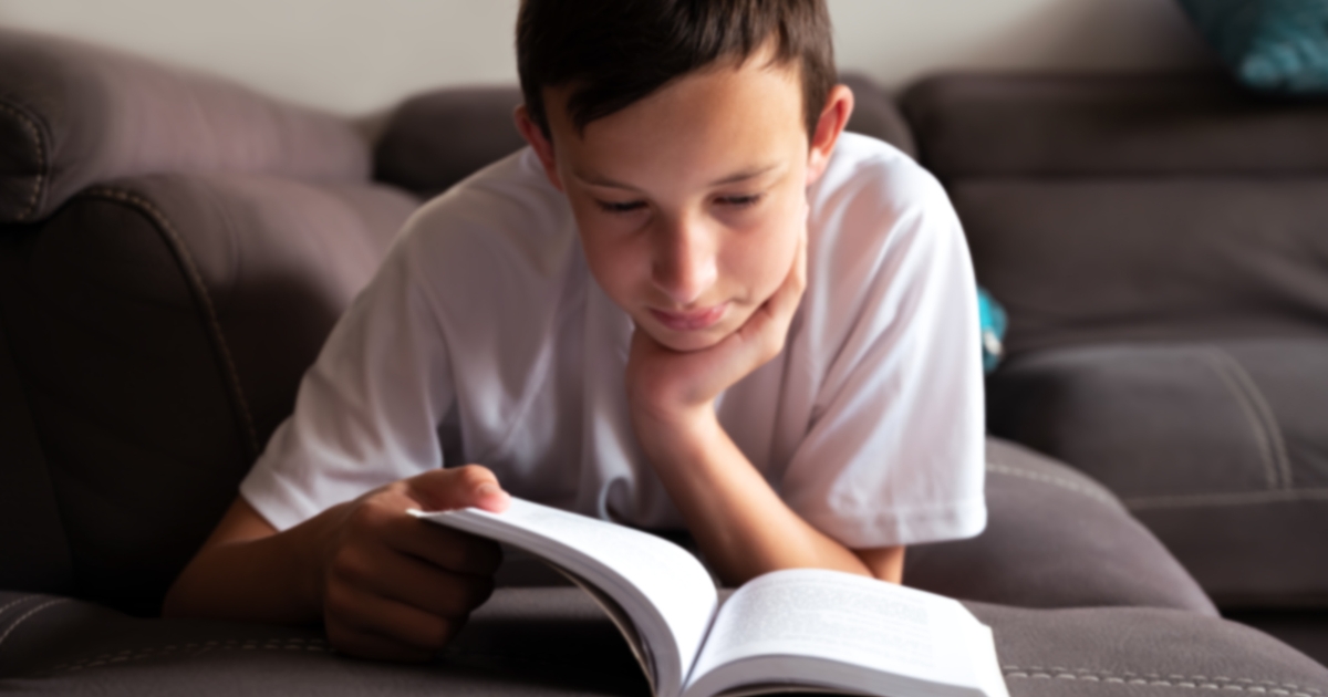 Middle school homeschool student reading a book on a couch, engaged in a literature curriculum.