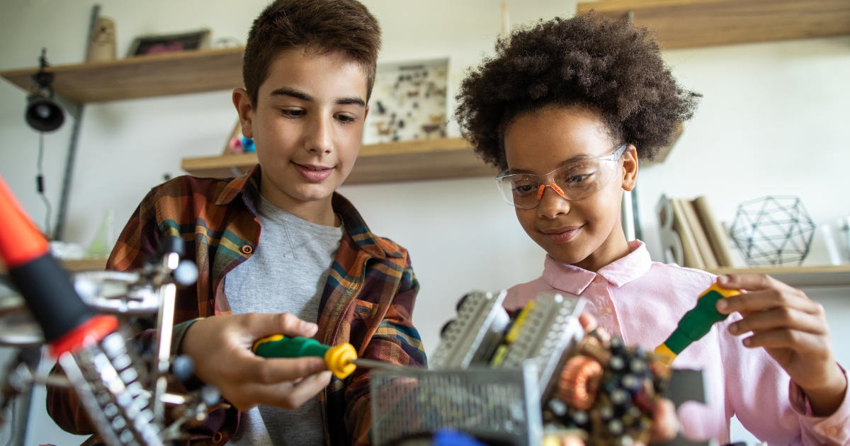 Two children working on a hands-on STEM project with tools and mechanical parts.