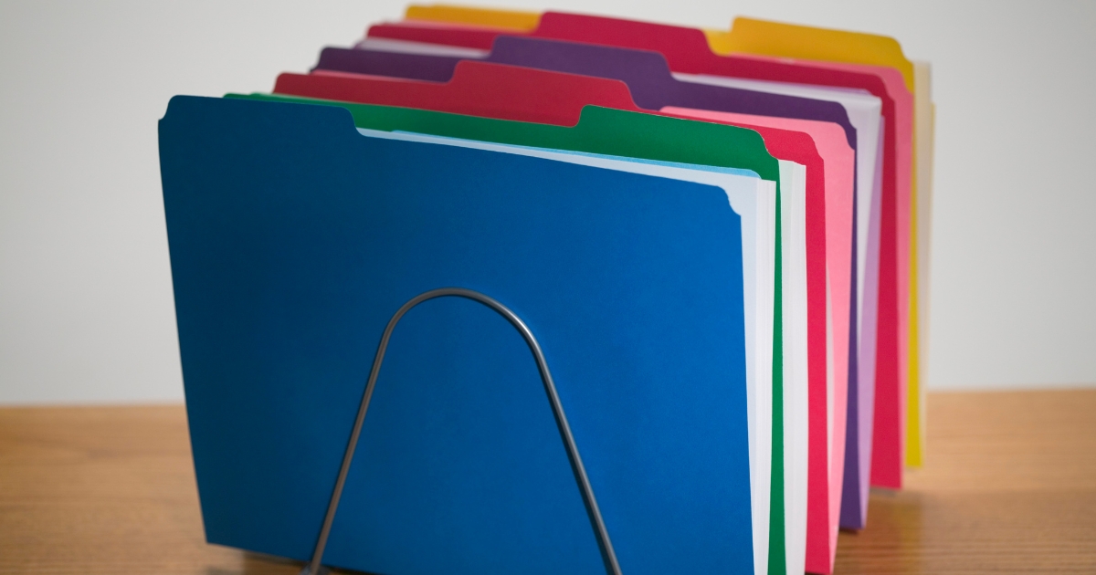 Color-coded file folders in a metal organizer for homeschool record keeping and organization.